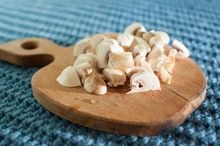 The process of cutting champignon mushrooms on a wooden cutting board on blue fabric knitted background close-upの写真素材