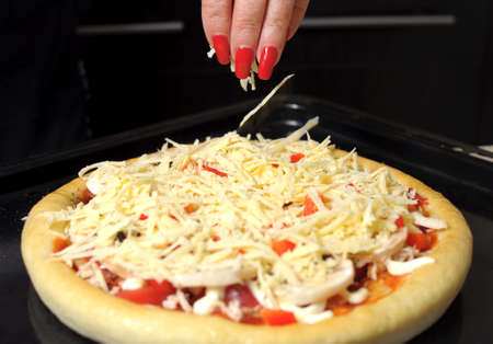 A female hand sprinkles a pizza with grated cheese close-up. Selective focus.の写真素材