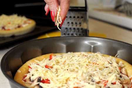 A female hand sprinkles a pizza with grated cheese close-up. Selective focus.の写真素材