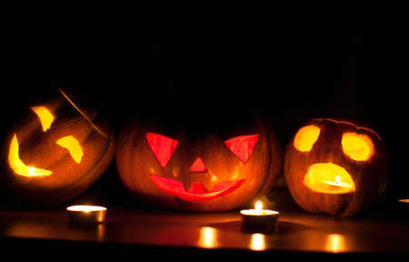 Scary halloween pumpkin and melon jack-o-lanterns on black background lit with small round and star candles. Selective focus, bokeh.の写真素材