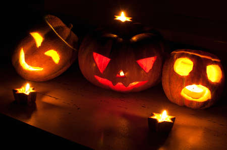 Scary halloween pumpkin and melon jack-o-lanterns on black background lit with small round and star candles. Selective focus, bokeh.の写真素材