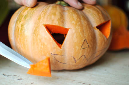 Halloween pumpkin cutting process, process of making Jack-o-lantern. Male hands with knife, leftovers of pumpkin on the kitchen table. Selective focus and bokeh.の写真素材