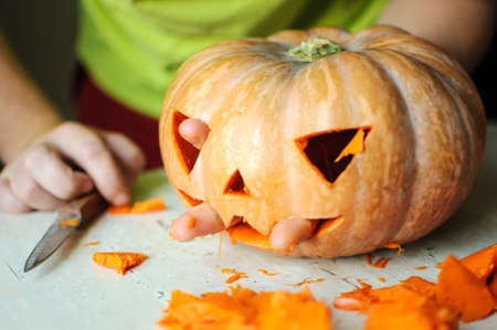 Process of making Jack-o-lantern. Funny picture of Halloween pumpkin monster face with male fingers. Selective focus and bokeh.の写真素材