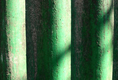 Sunlit green painted wavy slate background. Shabby wavy slate texture with unevenness and dust