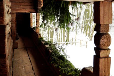 White and green holiday decoration at a porch of an old carving log cottage with spruce branches and white Christmas balls.の写真素材