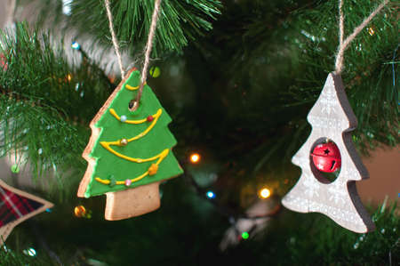 A cookie and a wooden toy in the form of a Christmas tree are hanging on a branch of Christmas tree. Selective focus, bokeh. Holiday background or image.の写真素材