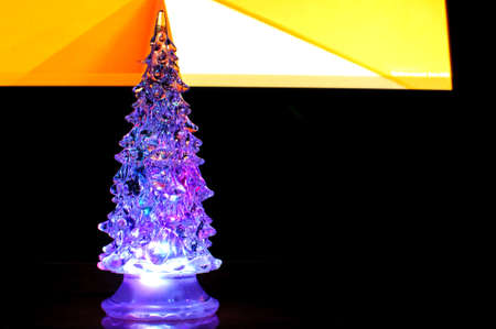 A small lighting Christmas tree on the contrast dark and orange geometric background. Selective focus, reflections, geometric lines. Abstract colorful Christmas background.の写真素材