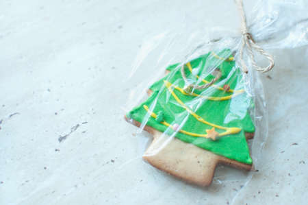 A green glaze Christmas gingerbread cookie in the shape of Chrismas tree in a cellophane packing on a wooden table. Close-up, selective focus, bokeh, copy space. Christmas gift concept.の写真素材