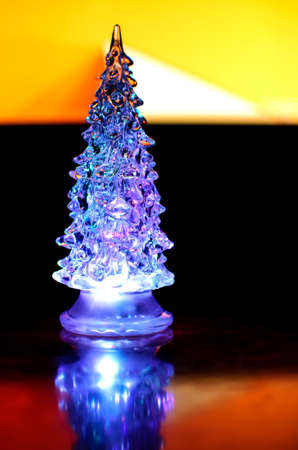 A small lighting Christmas tree on the contrast dark and orange geometric background. Selective focus, reflections, geometric lines.の写真素材