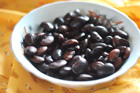 Black beans in a white ceramic bowl on the background of yellow clothの写真素材