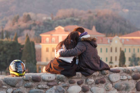 boys kissing each other while sitting on a wall at sunsetの写真素材