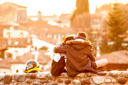 boys kissing each other while sitting on a wall at sunsetの写真素材