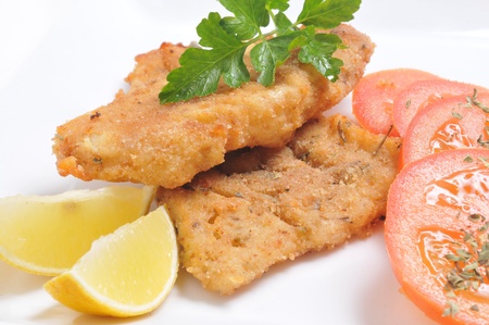 Fish schnitzel served with tomatoes, parsley, and lemons.の写真素材