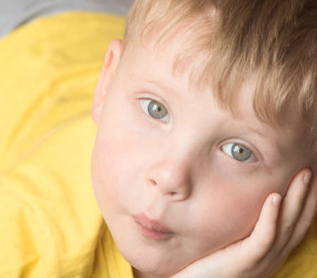 Little boy is chewing a candy with his hand under his cheekの写真素材