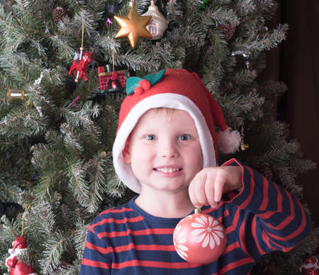 Boy in red hat having christmas ball and smilingの写真素材