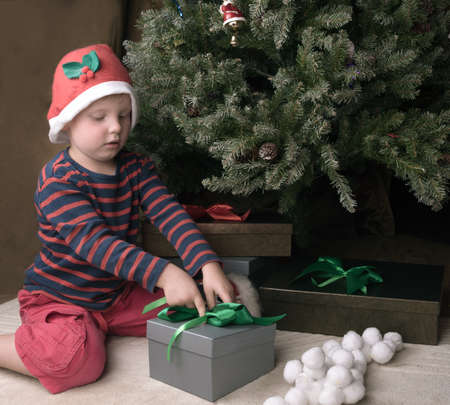 Boy is opening grey christmas present with green ribbonの写真素材