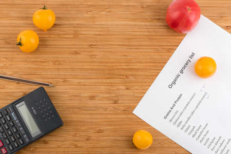 Purchase list surrounded by a fresh tomatoes and calculator on old wooden tableの写真素材