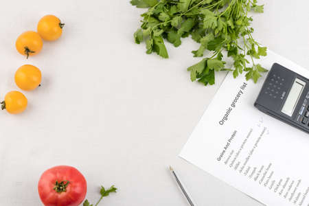 Purchase list surrounded by a fresh tomatoes and calculator on white backgroundの写真素材