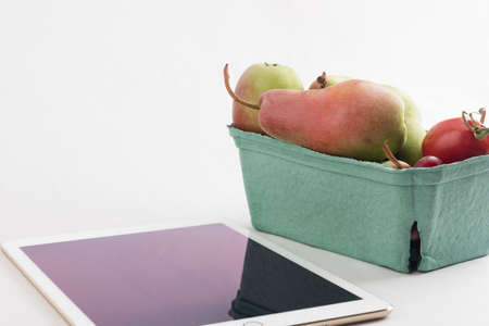 Fresh pears and tomatoes in a carton box and tablet pc on white backgroundの写真素材