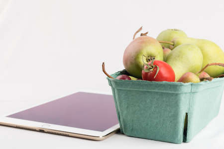Fresh pears and tomatoes in a carton box and tablet pc on white backgroundの写真素材