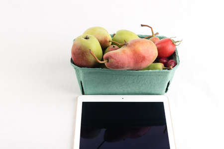 Fresh pears and tomatoes in a carton box and tablet pc on white backgroundの写真素材