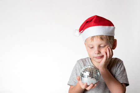 Cute boy with red Christmas hat on and disco ball in his handの写真素材