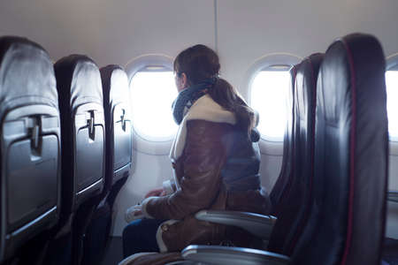 Young woman is on passenger seat at airplane, looking outside