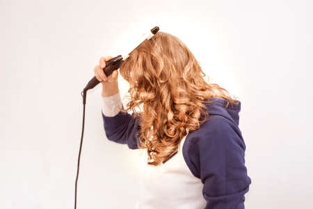 Young beautiful woman using modern hair curling  iron to make new stylish hairstyle.の写真素材