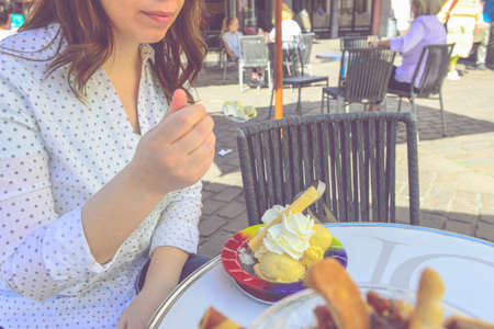 Caucasian happy woman holds spoon with ice cream, covered with  whipping cream and waffle. Cropped...