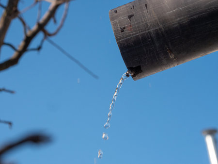 Water poured from black plastic pipe on blue sky backgroundの写真素材