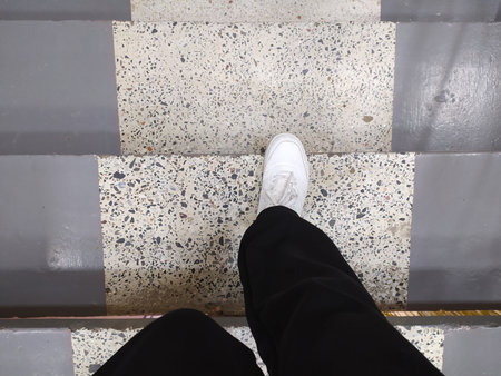 Legs in white sneakers and black pants walking down steps, top viewの写真素材