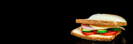 fresh sandwich with ham, cheese, bacon, tomatoes, lettuce, cucumbers and onions on a black backgroundの写真素材