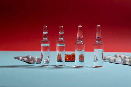 Glass ampoules and pills in blister pack on blue and red backgroundの写真素材