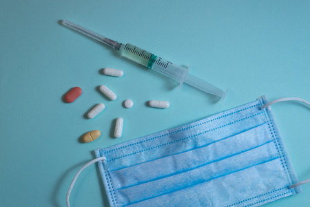 Pills, syringe and face mask lying on blue backgroundの写真素材