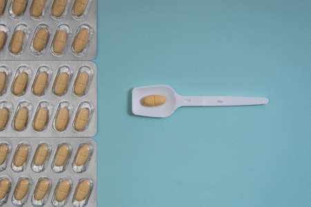 White, red and yellow pills on blue background with a hard shadowの写真素材