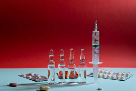Glass ampoules and syringe with medicine on blue and red backgroundの写真素材