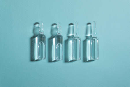 Glass ampoules with liquid medicine lying on blue background with hard shadowsの写真素材