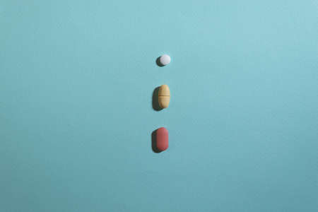 White, red and yellow pills on blue background with a hard shadowの写真素材