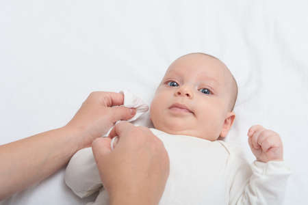 Mother hand cleaning baby ear and nose with a cotton swab. Baby taking care and hygiene concept.