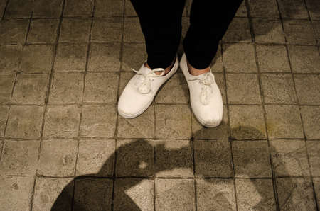 The shadow the hands of a man holding a camera on the concrete floor of an urban street and the...
