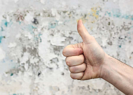 Hand showing gesture of agreement, forefinger up against old white wall background