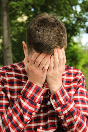 The guy in the plaid shirt wipes his face with his hands. The man is cryingの写真素材