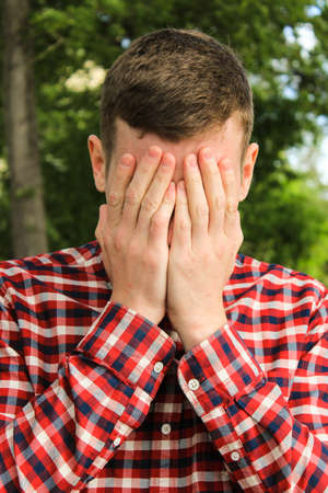 The guy in the plaid shirt wipes his face with his hands. The man is cryingの写真素材