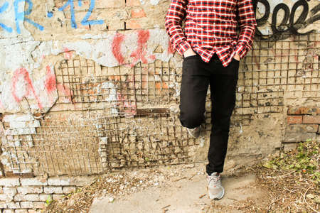 A guy in a plaid shirt is standing by the old wall in the parkの写真素材