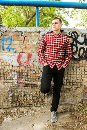 A guy in a plaid shirt is standing by the old wall in the parkの写真素材