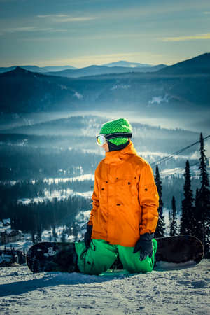 snowboarder sits on the slope and looks into the distanceの写真素材