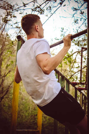 Guy pulling himself up on the crossbar, playing sports in the parkの写真素材