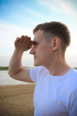 A guy in a white T-shirt is standing on the beach and looking into the distanceの写真素材