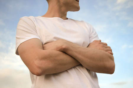 The guy in a white T-shirt is standing against the blue sky with his arms crossedの写真素材