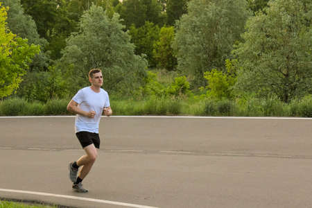 A guy runs in the summer on an asphalt road, doing sportsの写真素材